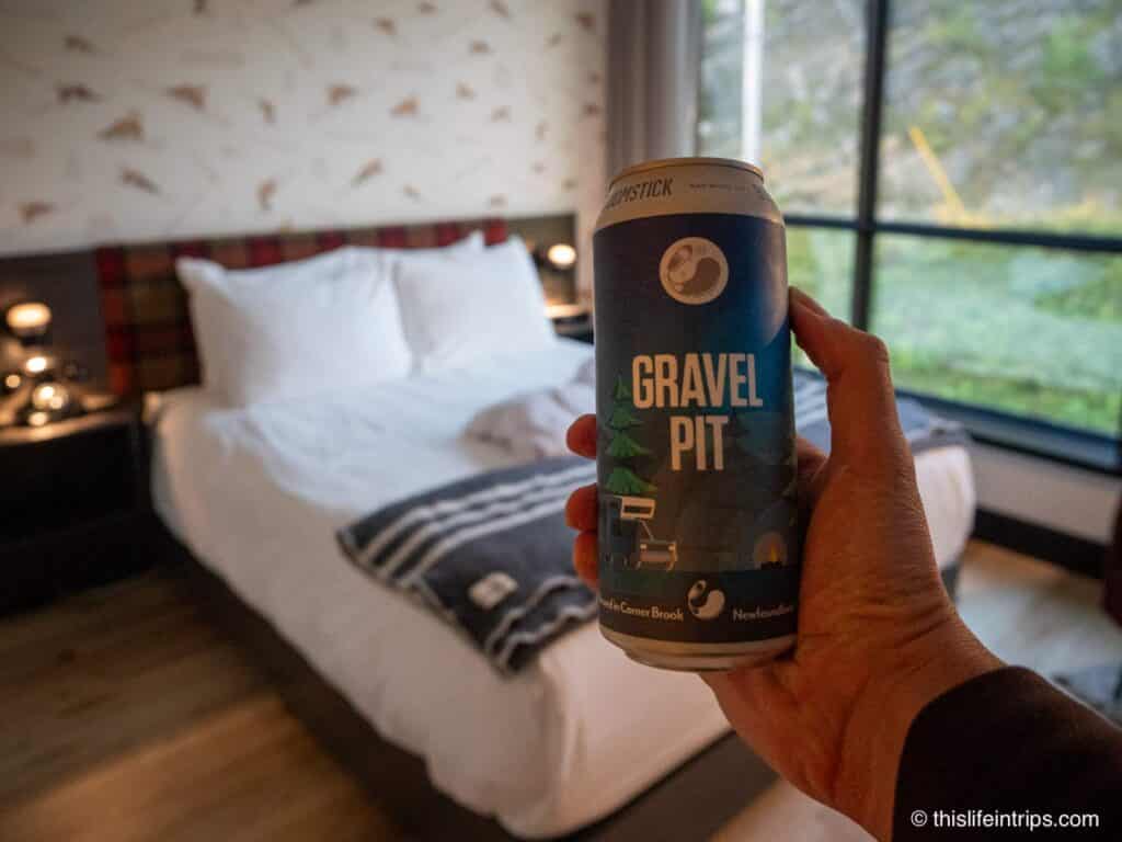 hand holding up a Gravel Pit beer in front of a bed at the Hew and Draw Hotel in Corner Brook Newfoundland