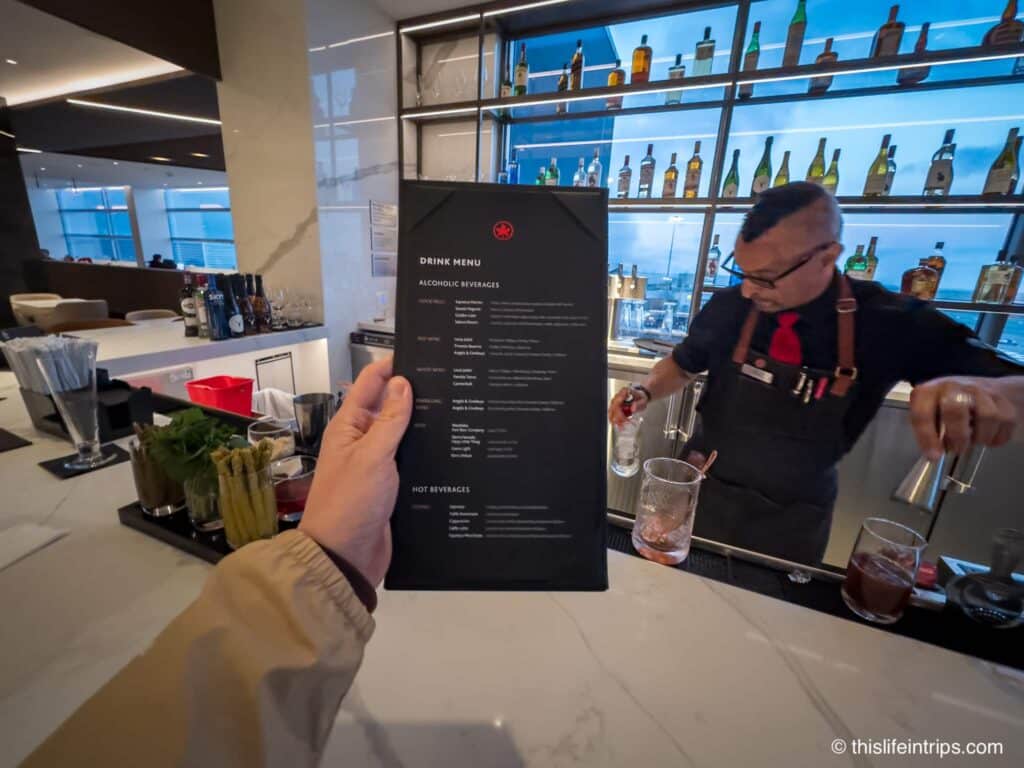 Hand holding up Air Canada SFO lounge menu. Bartender making drink in background