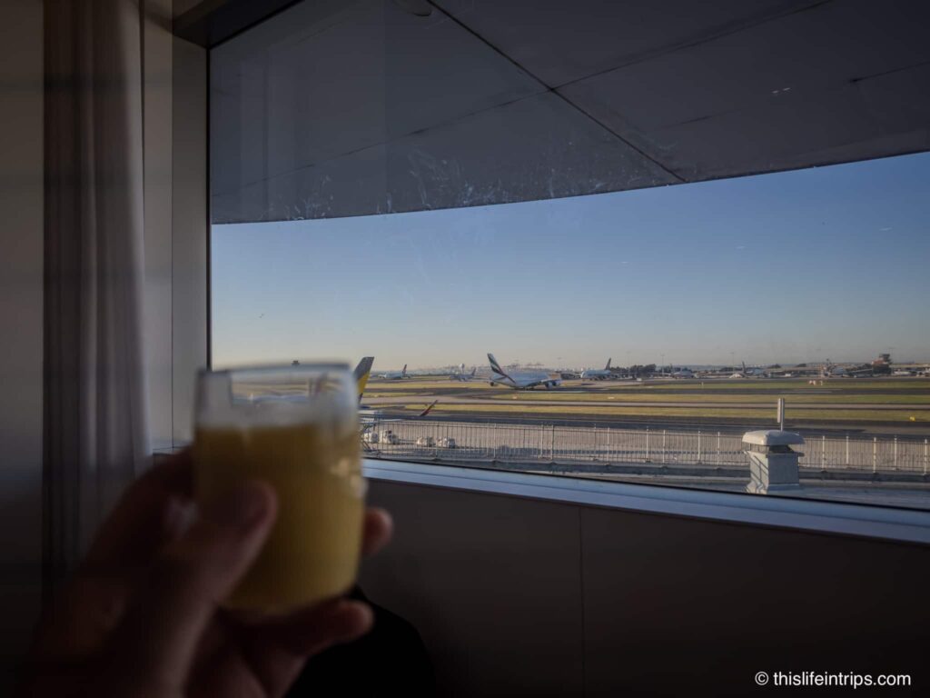 hand holding up a smoothie looking at the tarmac from the Air New Zealand Lounge Sydney entrance