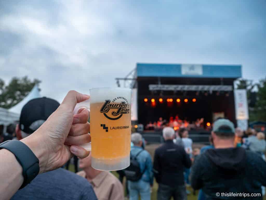 hand holding up a beer in front of a stage at the Baie Comeau beer festival