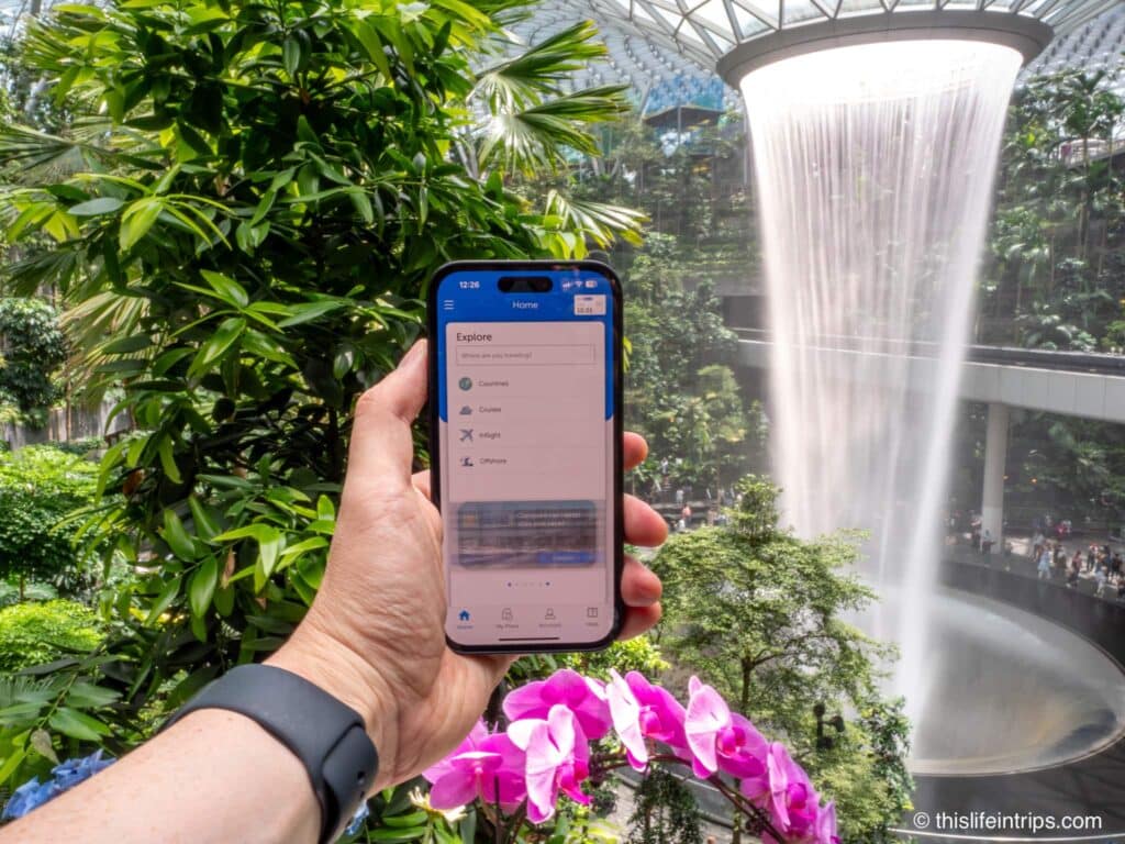 Hand holding up cell phone in front of the Jewel waterfall in Singapore during a Gigsky review