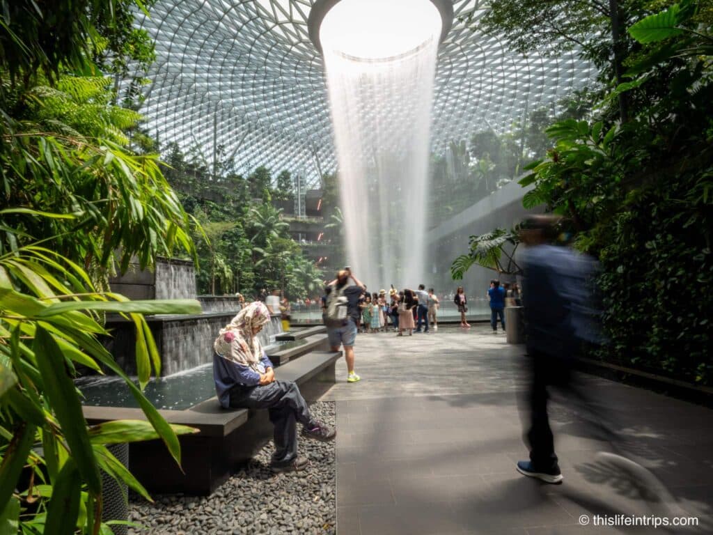 Man walking past seated women at the Jewel waterfall in Singapore
