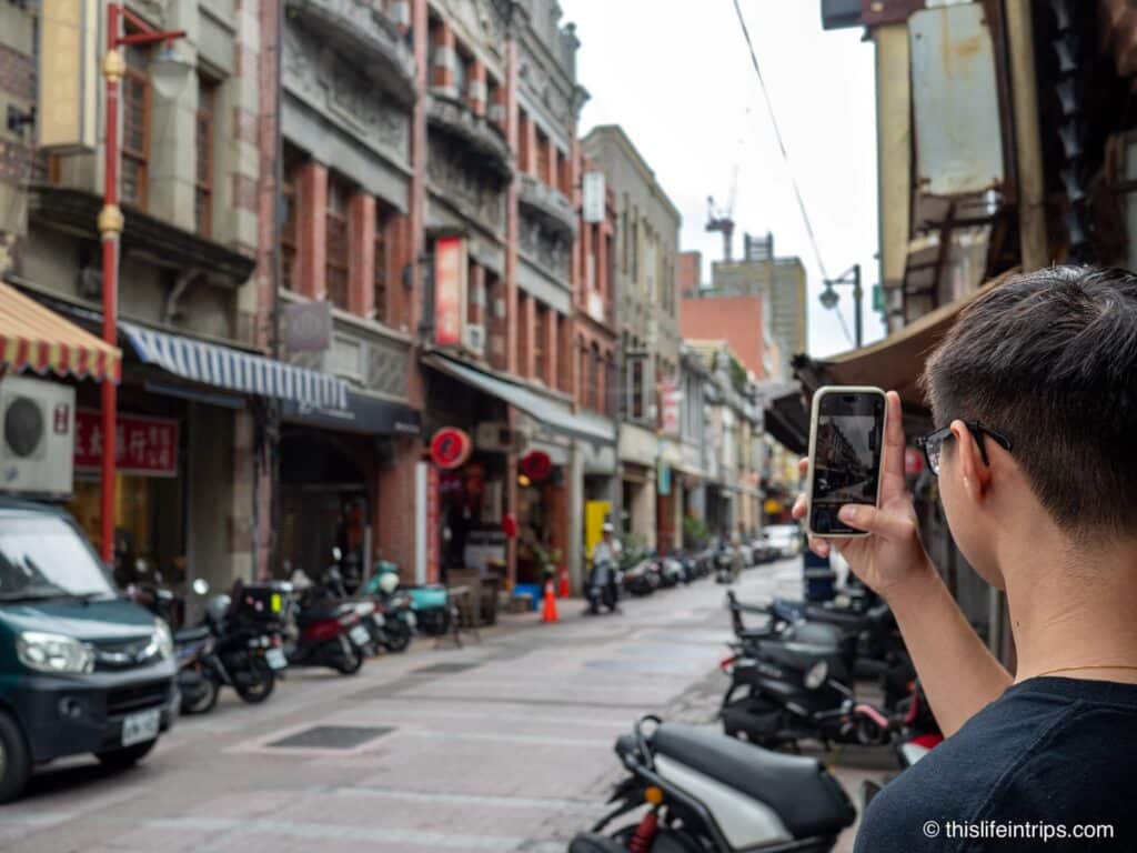 Man photographing Dihua Street in Taipei with iphone