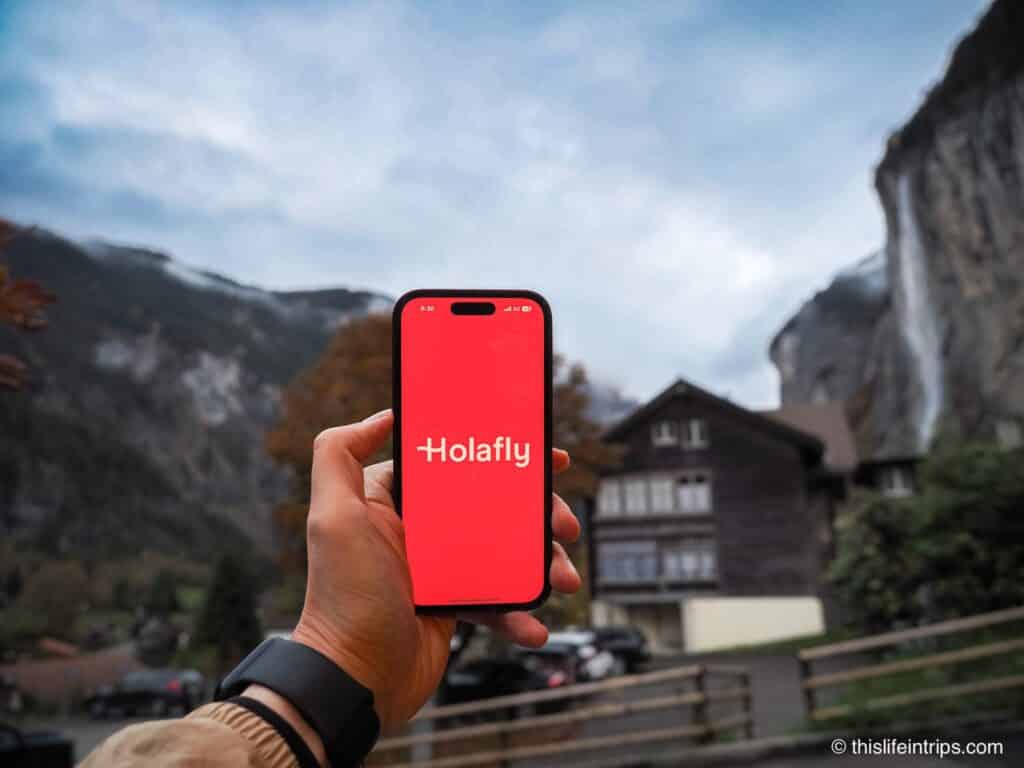 Hand holding up iPhone with Holafly eSIM app splash screen in front of waterfall