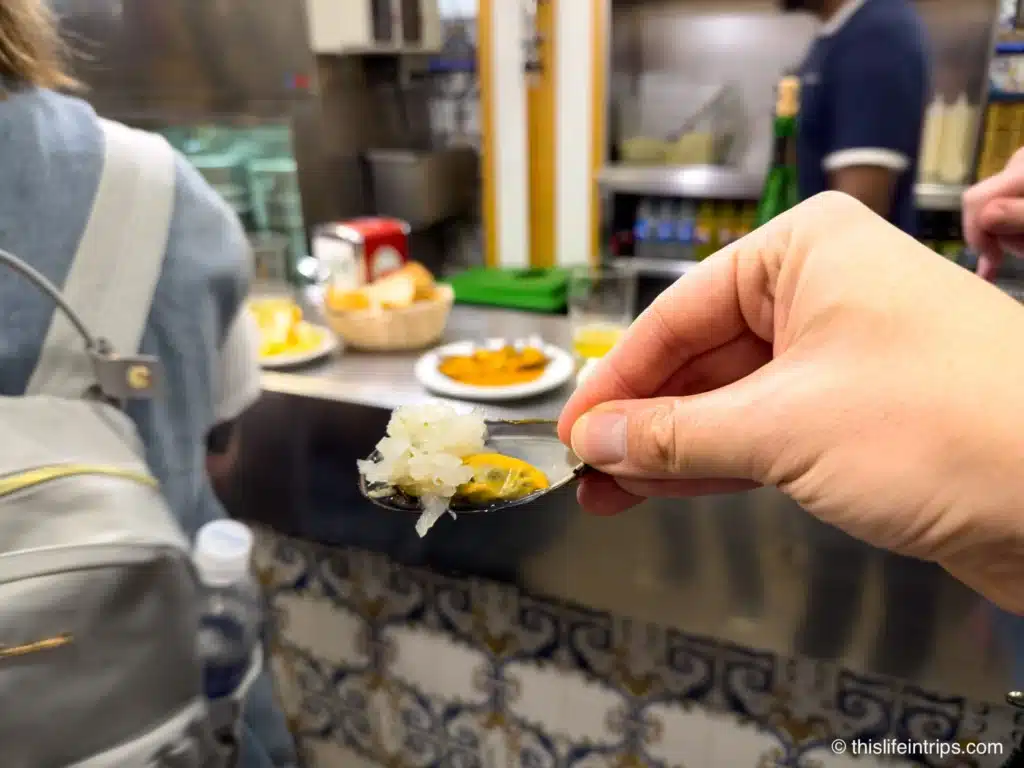 Hand holding up a muscle shell piled with white onions inside a San Sebastian pincho bar