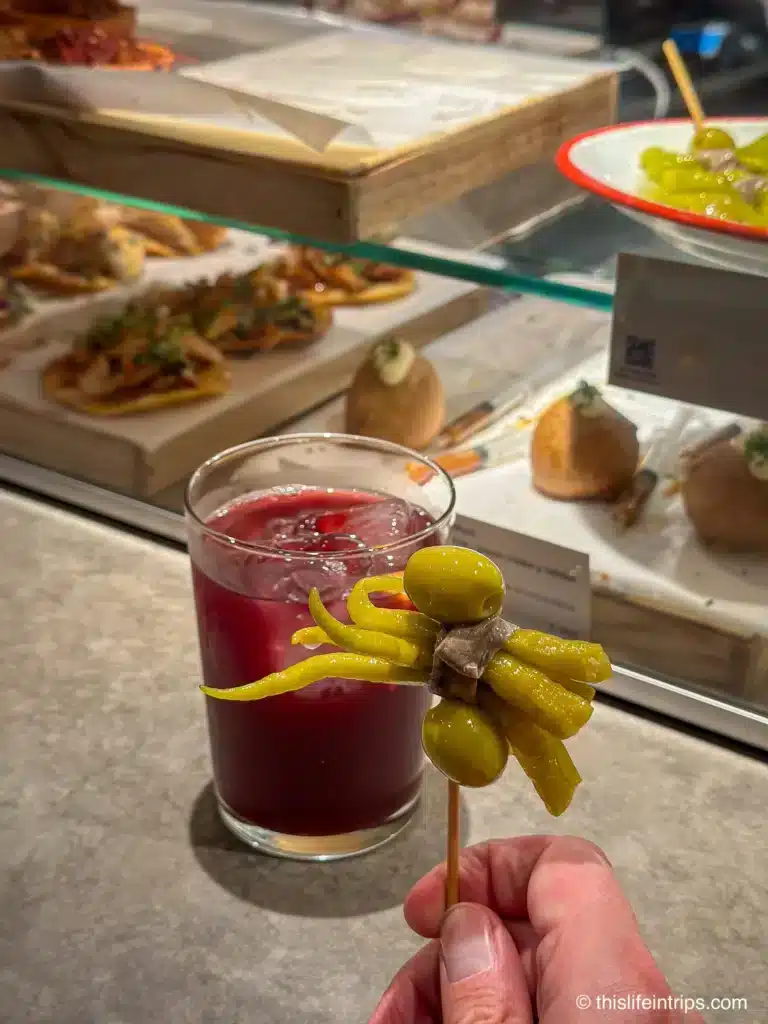 Hand holding up a Gilda Pintxos in San Sebastian in front of a glass of sangria